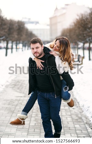 Close up photo of young healthy man holds his pretty girlfriend on the hands on background of winter snowy street. New Year and Christmas concept.