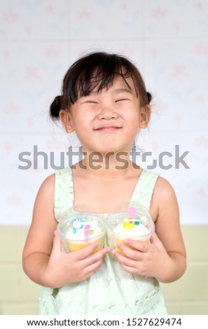Cute Asian child girl is smiling while holding cupcakes