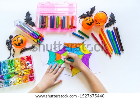 Child draws a rainbow cobweb. Drawing halloween Crayons and material for creativity. Autumn holiday.
