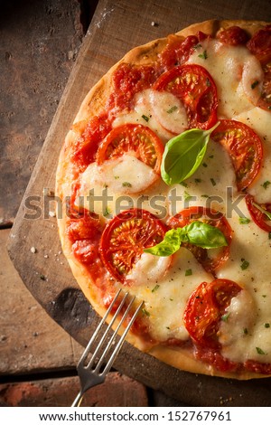 Overhead view of an appetizing tomato pizza with golden melted cheese and basil served on an old wooden board