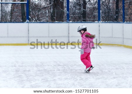 Beautiful girl having fun in winter park, balancing while skating at ice rink. Enjoying nature, winter time. Baby takes her first steps in figure skating