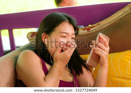 lifestyle portrait of young beautiful and happy Asian Korean student girl using internet social media app networking with hand phone outdoors at cool cafe smiling cheerful laughing online dating