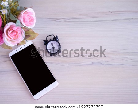 Blank screen phone on wooden desk with alarm clock  on wooden desk,selective focus.