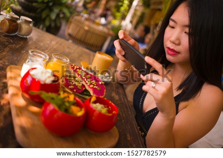 young and beautiful Asian woman takes photography of food on table with phone for internet blog. Chinese girl posting online photo for vegetarian, healthy and organic social media