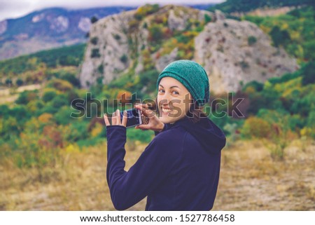 Smiling young traveller woman taking outdoor photo of autumn mountain landscape by her smart phone.