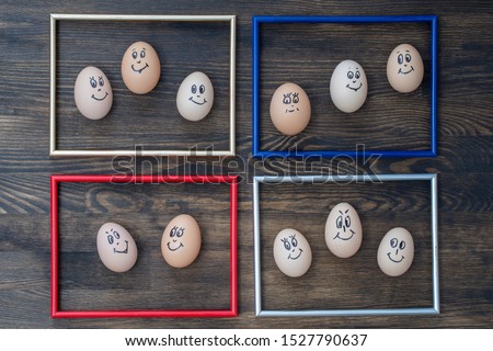 Picture frame and many funny eggs smiling on dark wooden wall background, close up. Eggs family emotion face portrait. Concept funny food
