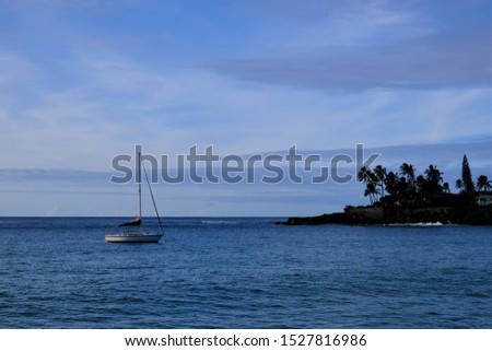 Sailboat anchored in Waimea Bay with a background of a surf spot off a point of land.