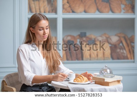 Woman is heaving breakfast with croissant and coffee in the morning. Very beautiful girl with long blonde hair having lunch in a bakery