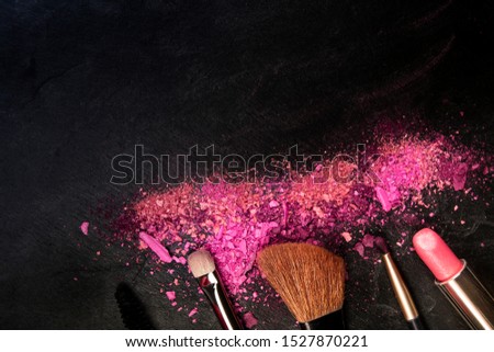 Make-up brushes and lipstick with broken cosmetics, overhead shot on a black background with copy space, a beauty design template for a makeup banner