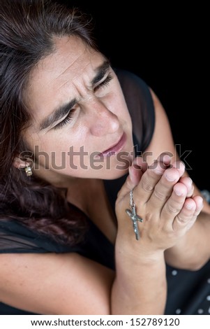 Dramatic portrait of an hispanic woman praying with a small crucifix (isolated on black)