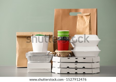 Different packages on table against color background. Food delivery service Royalty-Free Stock Photo #1527912476