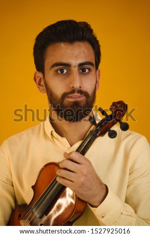young male artist violinist sitting with a violin and a bow on a yellow background and posing for the camera in the studio. armenian man looking at the camera in a yellow shirt