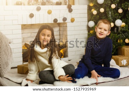 Happy little kids decorate Christmas tree in beautiful living room with traditional fire place. Children opening presents on Xmas eve.