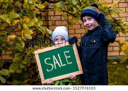 Two boys point to the inscription on the plate. Sign for advertising in the hands of children. The boys laugh and smile. Autumn sales, discounts, cheap prices. Autumn came, yellow leaves.