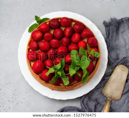 Cheesecake with fresh strawberries and mint on white plate on gray concrete background. Square image. Top view.