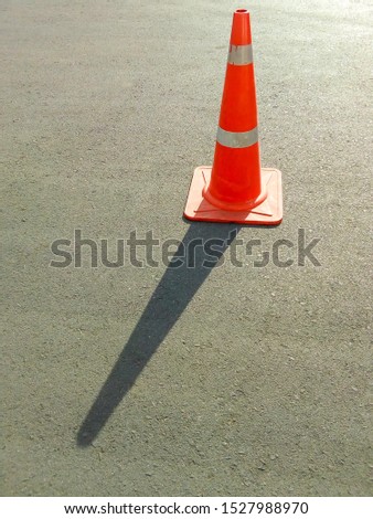 ฺBright orange traffic cone standing with shadow on dark asphalt