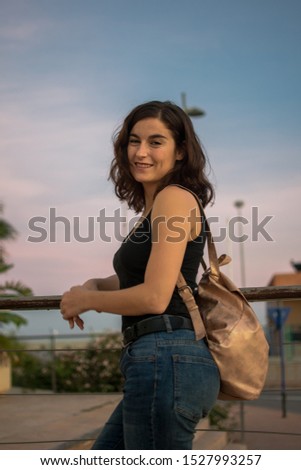 Stock photo of a woman looking at camera at sunset, the sky is in background. Lifestyle concept.