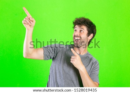Young crazy man pointing, proud and happy, looking shocked and surprised on green background
