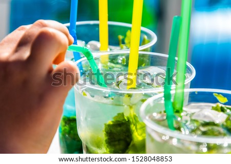 soft cocktail in plastic cups with ice and mint. cocktail tube in hand