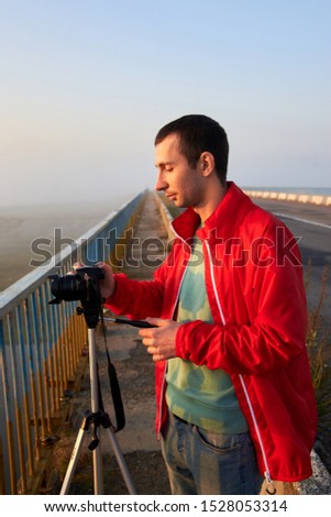 A man on a bridge over the river that photographs a sunrise on a foggy early morning.