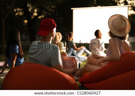 Young couple with popcorn watching movie in open air cinema. Space for text Royalty-Free Stock Photo #1528060427