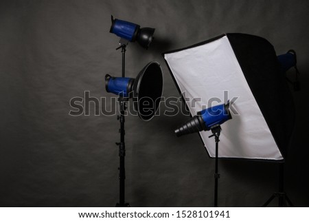 Modern photography equipment on the gray paper background: flash lights, softbox, reflector and snoot on stands