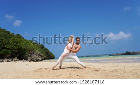 a pair of young acrobats on the ocean posing on the beach.acrobatic elements support on the background of a tropical beach. athletic beautiful couple in white.