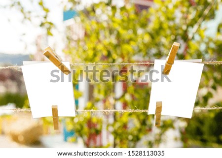 Blank photographs hanging on clothesline against blue sky over green grass