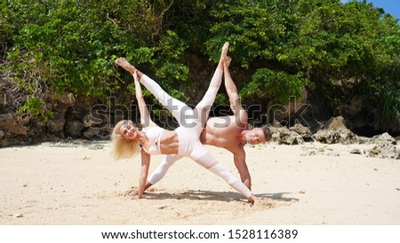 beautiful blonde girl and handsome man in white on the Pacific coast in Asia is engaged in acro yoga, pair acrobatics. duo acrobats circus performers dancers on the beach twine