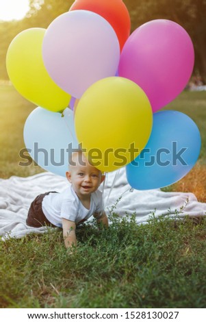 Happy little child near colorful balloons on the field.
