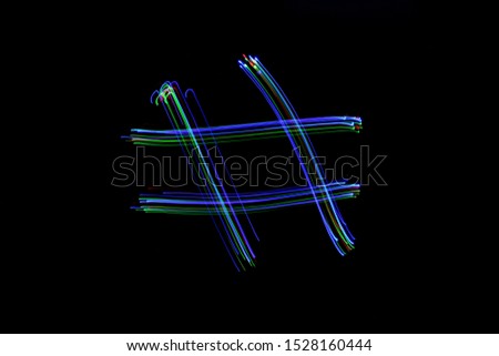 Long exposure photograph of a hash tag symbol in neon colour in an abstract swirl, parallel lines pattern against a black background. Light painting photography.
