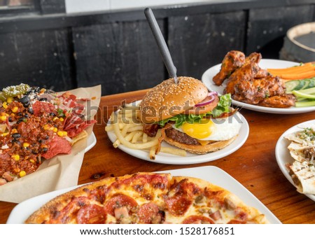 Unhealthy food served in an American bar and grill. Delicious cheeseburgers, meat lover's pizza, spicy nachos, and buffalo wings; food that will ruin a diet.