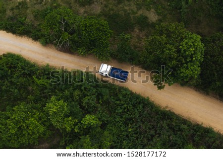 Aerial view, construction truck is transporting materials through a dirt path surrounded by trees. Activity machine in building business. Top view from drone.