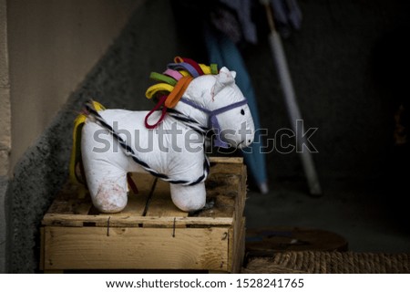 A closeup shot of a cute white horse toy with a colorful mane and a tail on a wooden box