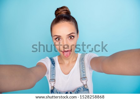 Self photo of charming cute attractive playful girlfriend showing you her tongue while isolated with blue background