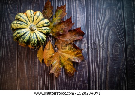 Orange and brown Autumn leaves with a pumpkin on a wooden background.
