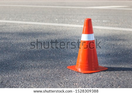 Red orange cone with a white stripe on the asphalt road. Drive safety and constructions concept.