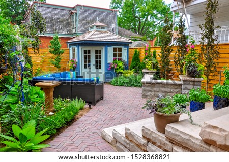 Contemporary with traditional elements, this beautiful small urban backyard garden features a seat wall, red brick paver herringbone patio, high end shed,  and mixed planting for colour and privacy. Royalty-Free Stock Photo #1528368821