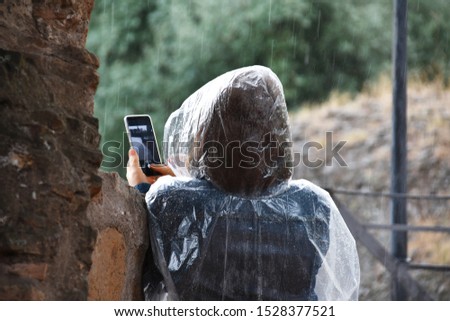 Woman taking pictures using cell phone in the rain