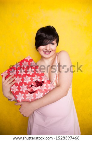 happy Female holding in hands big gift with ribbon. Adult girl with red present on yellow studio background.