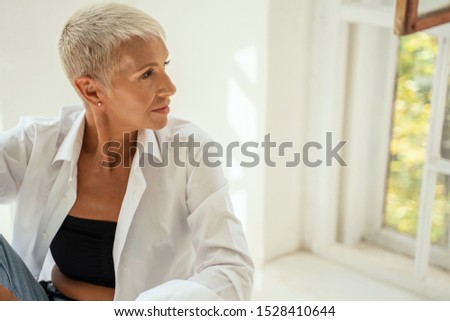 Stylish haircut. Profile photo of cute female that sitting on the foreground, being deep in thoughts