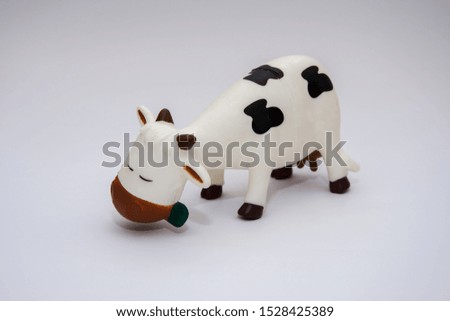 Toy cow with spots on a light background, the animal chews grass with pleasure closing his eyes
