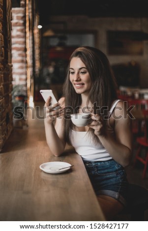 Woman using phone and drinking coffee in a cafe.