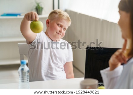 Fat boy doesn't want an apple. Overweight child at a nutritionist appointment. Healthy food, diet and weight loss.