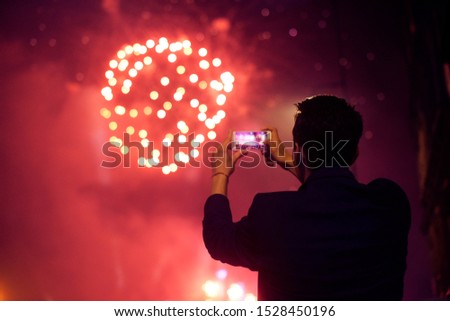 A man makes a photo of a salute on the phone. Holiday, fireworks. Application for processing photos.