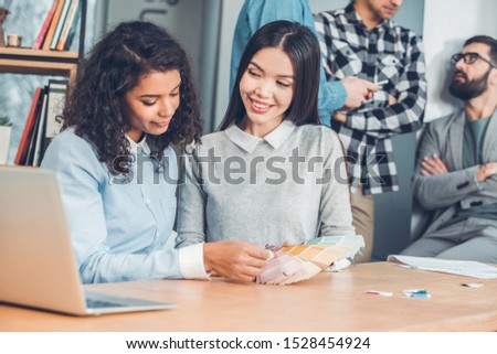Young business people working together at office two women designers sitting at table holding palette choosing color concentrated