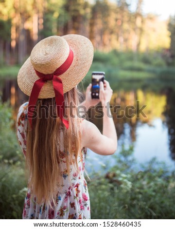 Woman wearing straw hat and taking photo on smartphone in the forest