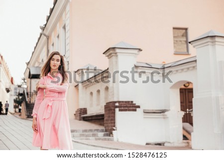 Beautiful confident girl in pink dress, she walks through the beautiful streets of the city, long beautiful hair, delicate makeup, urban style.