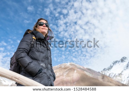 One young trekker girl looking at views at the outdoors inside a wild scenery surrounded by Andes mountains range and with her silhouette cut out over the blue and cloudy sky, an idyllic adventure