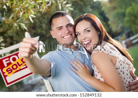 Mixed Race Excited Military Couple with New House Keys and Sold Real Estate Sign Outside.